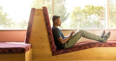 Black student reclined and working on computer