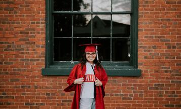 Young female college graduate in red cape and hat outside