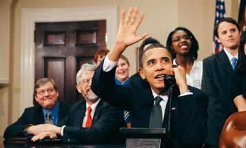 President Obama on the phone waving surrounded by staffers