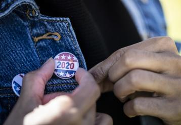 Black voter adjusting a 2020 flag pin on their jacket lapel
